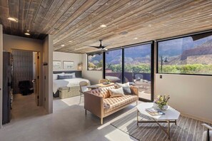 A modern interior with a wooden ceiling, a sofa, a bed, and large windows offering a view of a canyon. - Panoramic Zion Loft | Unit 2 (Springdale)
