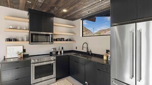 Une cuisine moderne avec des meubles de couleur sombre, des appareils électroménagers en acier inoxydable et un plafond en bois.