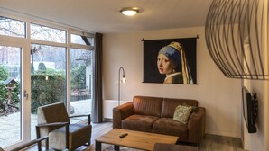 Una sala de estar con un sofá, una mesa de centro y un televisor. Se ve una ventana grande con vistas al exterior.