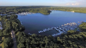 Vista aérea de un puerto deportivo rodeado de bosque frondoso, con barcos amarrados y una carretera que lo conecta.