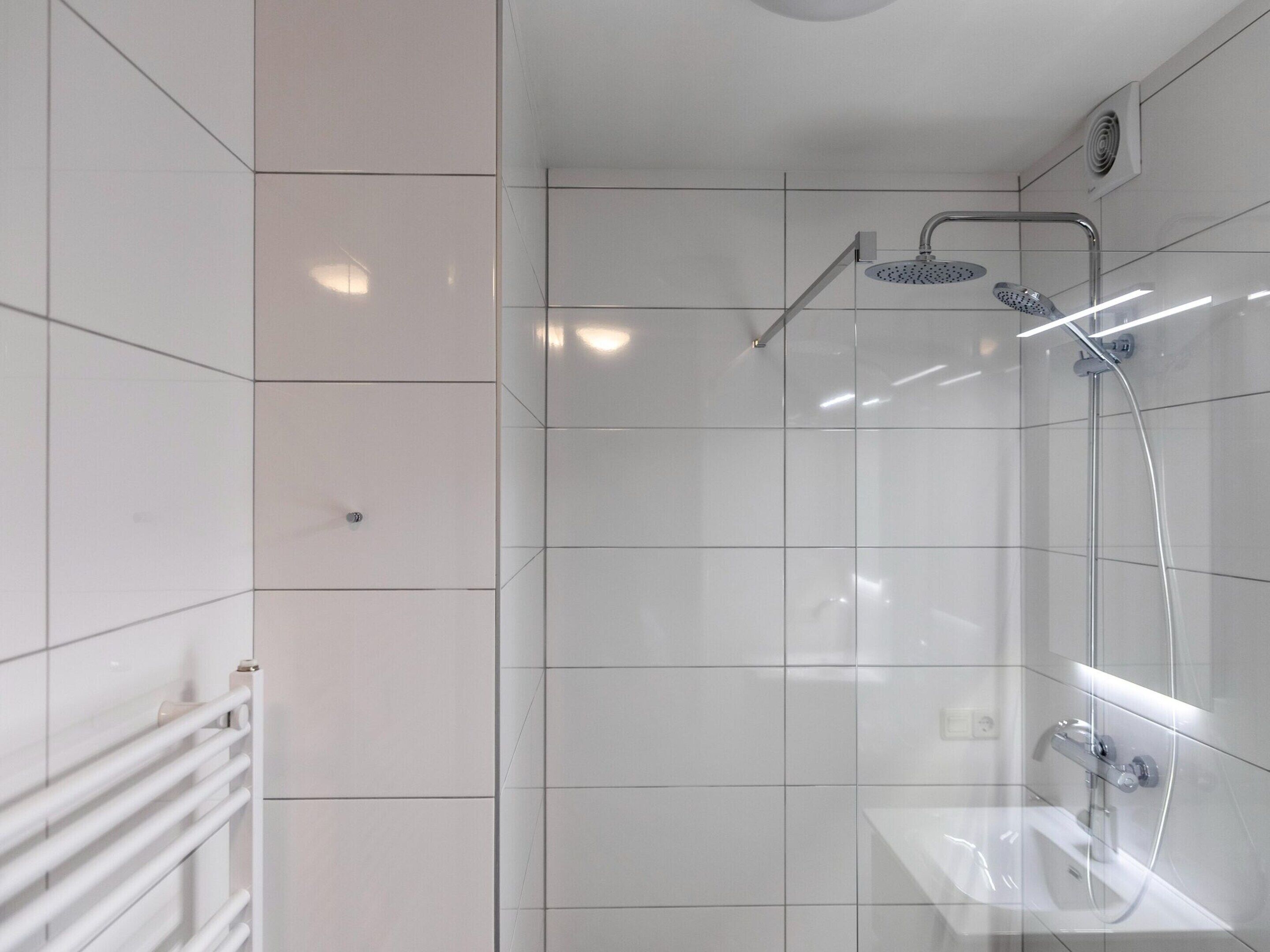 A modern bathroom with white tiles, a glass shower enclosure, and a white sink.