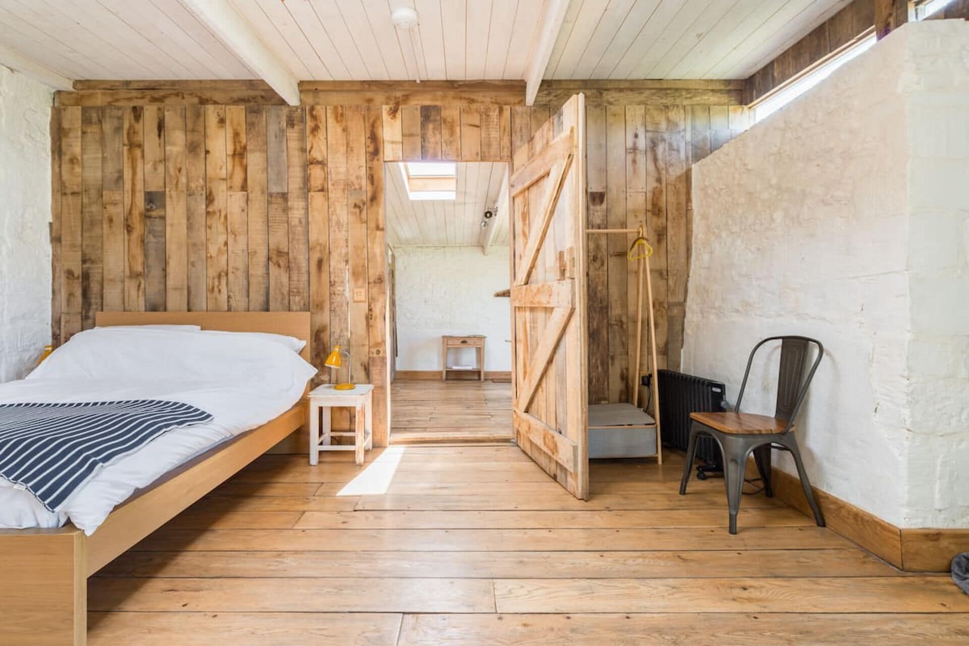 A rustic wooden room with a bed, a small table, and a chair.