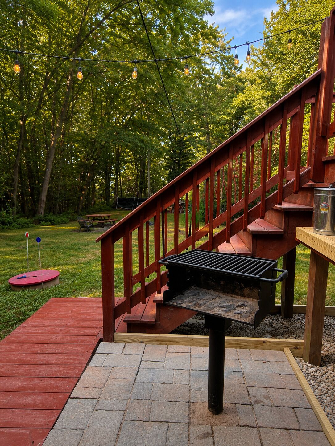 Una terraza de madera con una parrilla, una mesa de picnic roja y una escalera de madera.