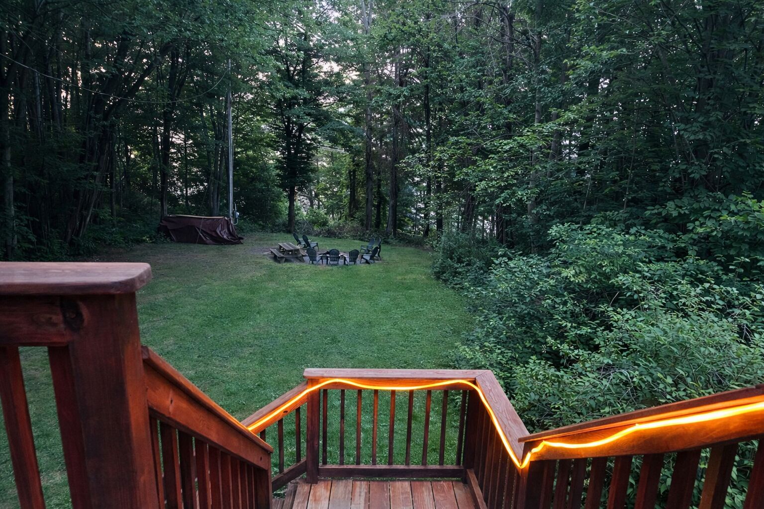 A wooden deck with a railing, a grassy yard, and a forested area in the background.