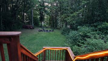 A wooden deck with a railing, a grassy yard, and a forested area in the background.