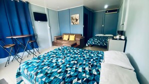 A hotel room with a large bed, a smaller bed, a sofa, a desk, and a TV. - Cabinas Arenal Home (La Fortuna)