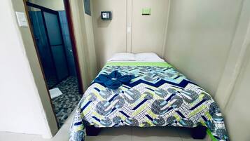 Una habitación pequeña y estrecha con una cama, una puerta y un aire acondicionado instalado en la pared.