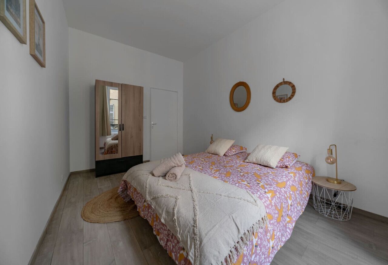 A bedroom with a bed, a wardrobe, a round mirror, and a small table with a lamp.