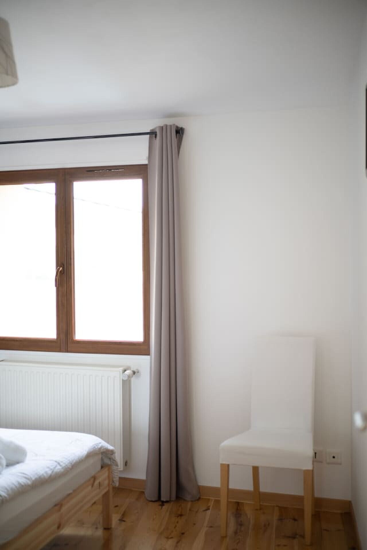 Una habitación con cama, radiador, ventana con cortinas y una silla.