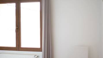 Una habitación con cama, radiador, ventana con cortinas y una silla.