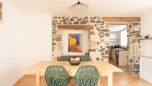 Un comedor con pared de piedra, un cuadro y una cocina al fondo.