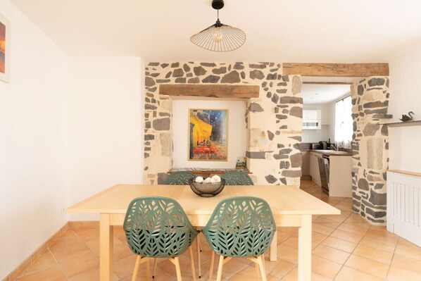 Un coin repas avec un mur en pierre, un tableau et une cuisine en arrière-plan.