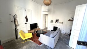 Olohuoneessa on sohva, keltainen nojatuoli, televisio, takka ja riippuvalaisin.