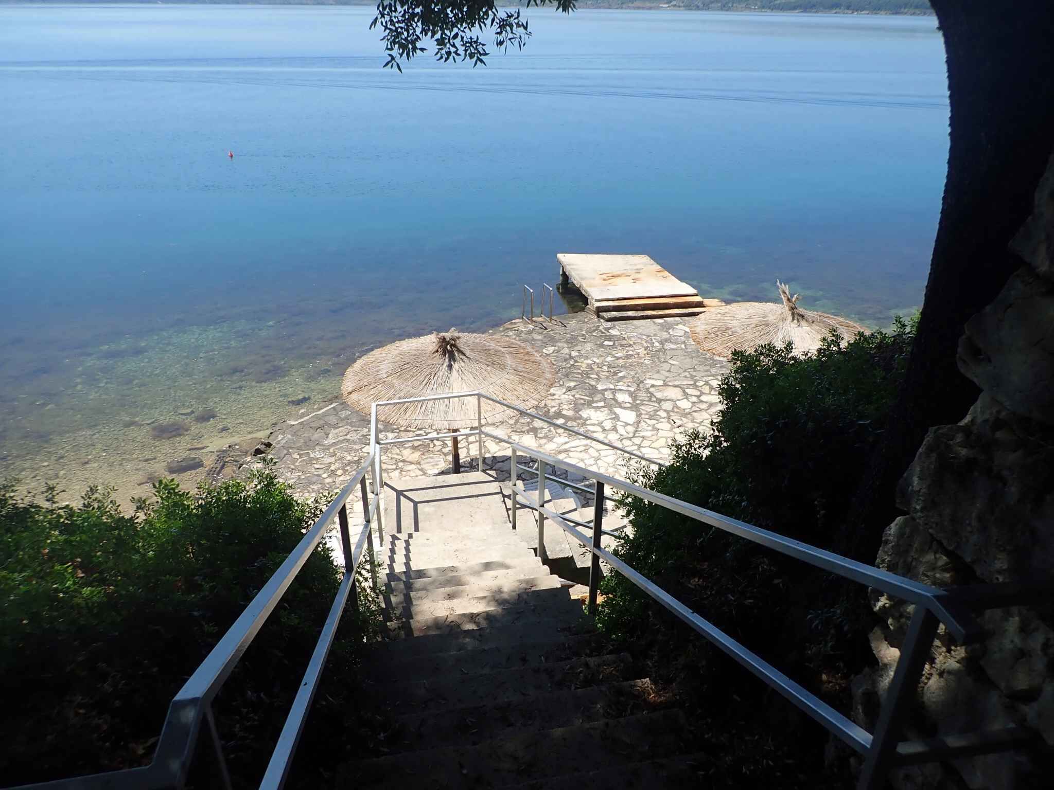 A staircase leading to a beach area with a thatched umbrella and a concrete platform.