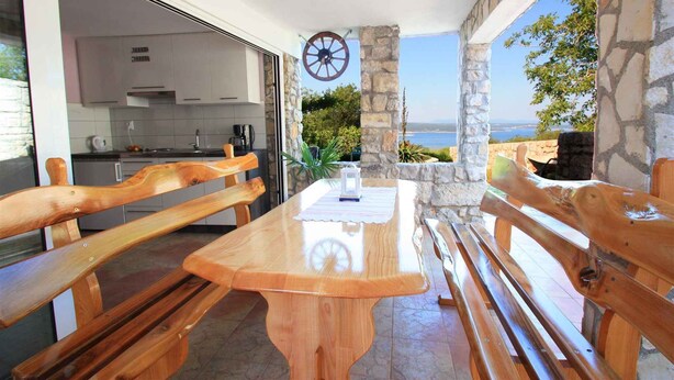 A wooden table with benches, a kitchen area, and a stone pillar with a wheel decoration.