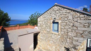 A stone building with a small window, a red roof, and a view of the sea.