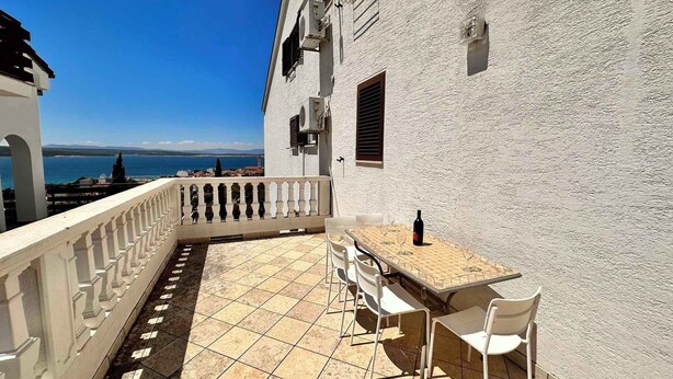 A balcony with a table and chairs, overlooking a body of water and distant land. - Holiday apartment with balcony and sea view (Crikvenica)