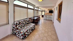 A narrow hallway with a sofa, a dining table with chairs, and a kitchen area with a TV. - Holiday apartment with balcony and sea view (Crikvenica)
