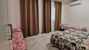 Een slaapkamer met twee eenpersoonsbedden, een groot bed, bruine gordijnen, een raam en een airconditioning.