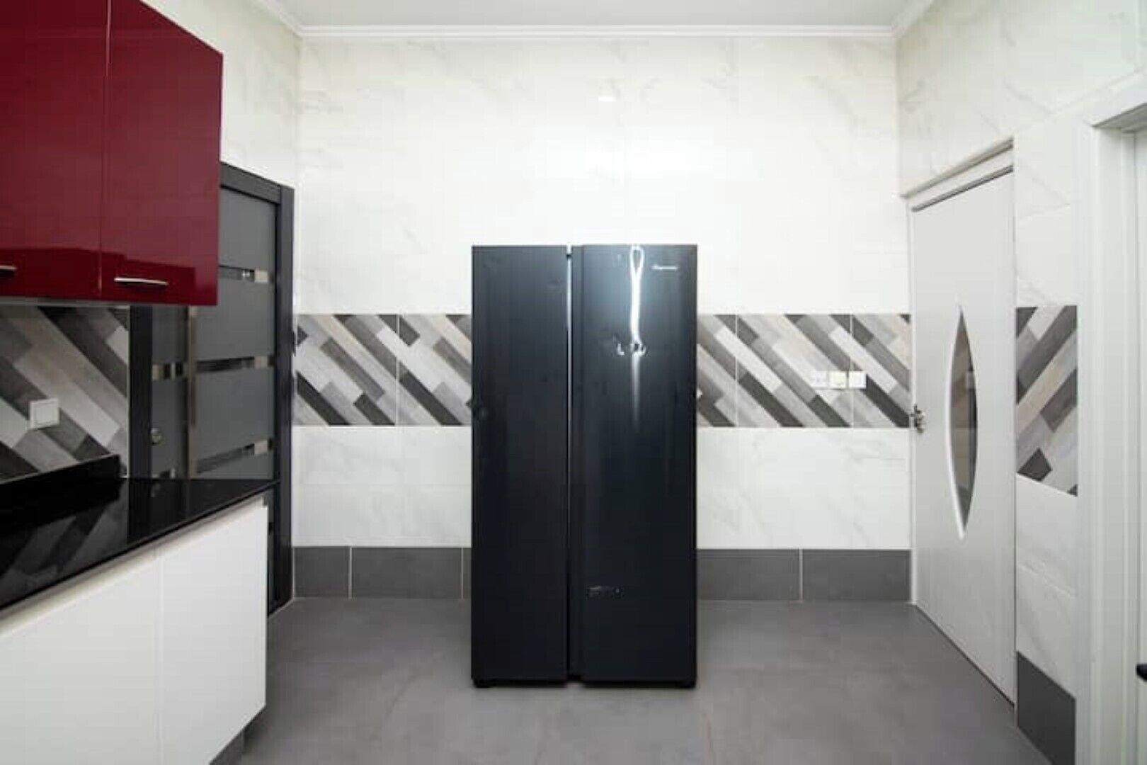 Uma cozinha compacta com uma geladeira preta, um armário vermelho e azulejos estampados nas paredes.