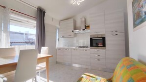 Une cuisine moderne avec un coin repas, comprenant une table et des chaises, un coussin coloré et une vue sur l’extérieur.