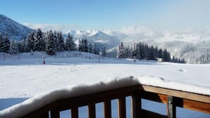 A snowy mountain landscape with a ski slope, trees, and a wooden structure in the foreground.