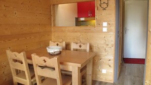 A wooden interior with a dining table and chairs, a small kitchen area with red cabinets, and a door leading to another room. - 10m from ski slopes, 3rd floor, balcony, tv, ski locker, 28m², Avoriaz (Avoriaz)