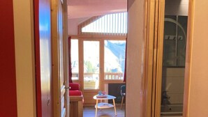 Ein schmaler Flur, der in einen Raum mit Holzboden, einem roten Stuhl, einem kleinen Tisch und einem Fenster mit Bergblick führt.