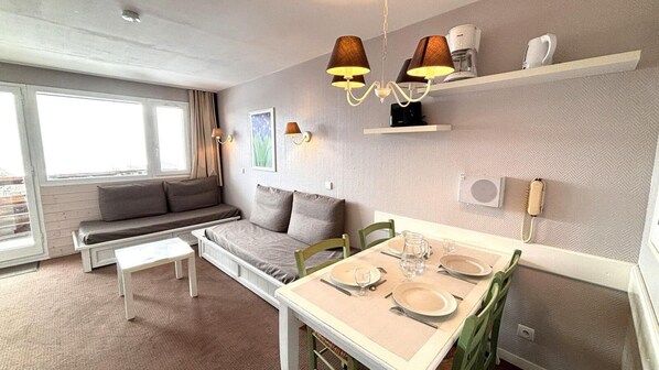 Een ruimtelijk ingerichte leefruimte met een bank, een eettafel en een kitchenette.