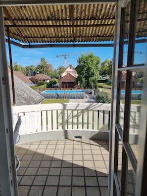 Een balkon met uitzicht op een zwembad, een witte hek en een gebouw met een bruin dak.