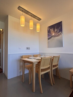 Uma sala de jantar com mesa e cadeiras de madeira, iluminação pendente, um quadro na parede e um lustre.