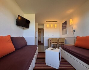 A compact hotel room with a bed, a desk, a chair, a television, and a lamp.