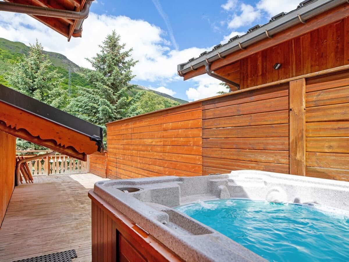 A wooden deck with a hot tub, surrounded by wooden walls and a mountain backdrop.