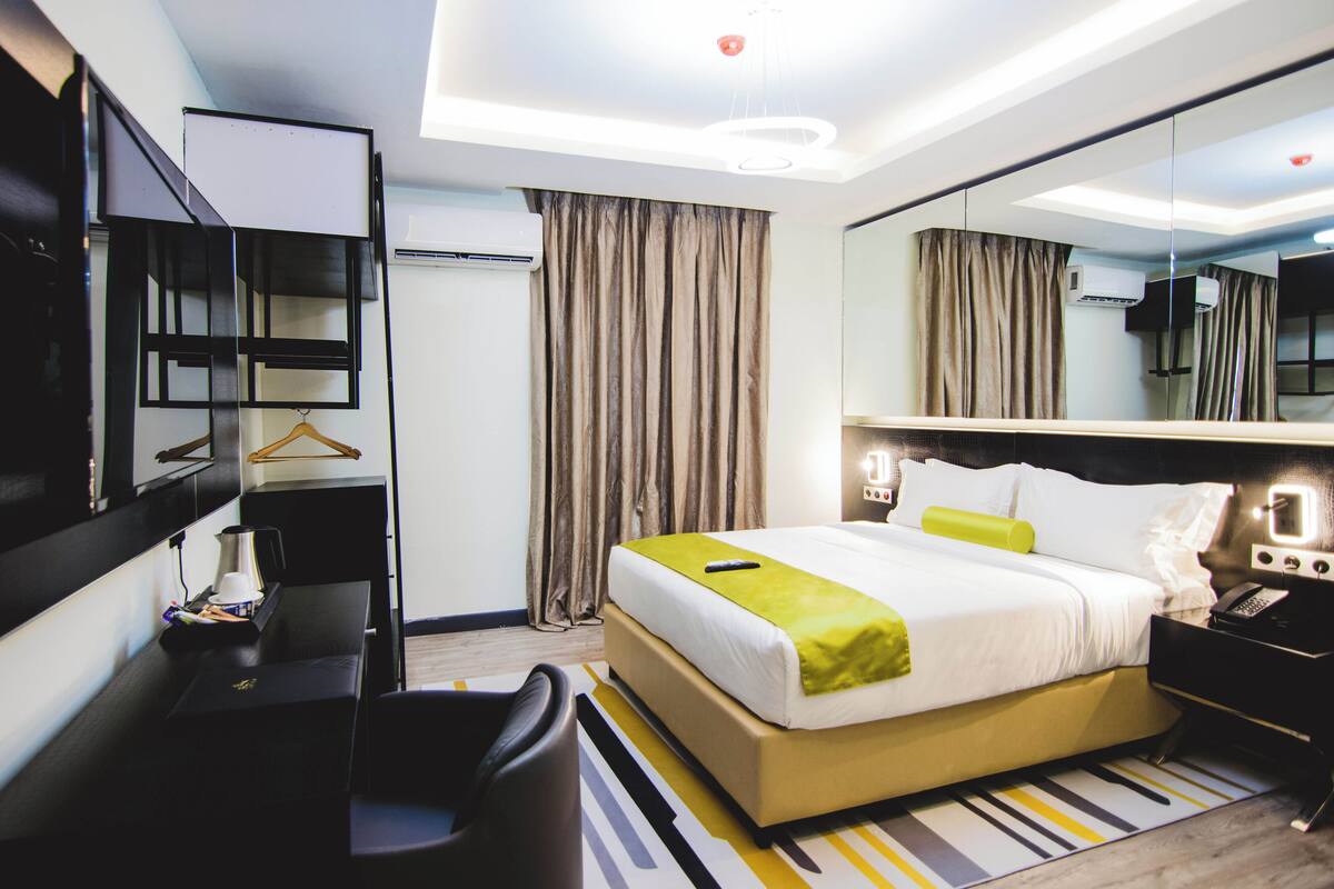 Une chambre d’hôtel moderne, dotée d’un grand lit, d’un bureau avec une chaise, d’un miroir et d’un luminaire suspendu.