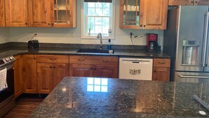 A kitchen with wooden cabinets, a granite countertop, a stainless steel refrigerator, and a coffee maker. - Peaceful Pines Hideaway  (Nottingham)