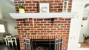 A brick fireplace with a "HOME" sign above it, flanked by white shelves and a small plant. - Peaceful Pines Hideaway  (Nottingham)