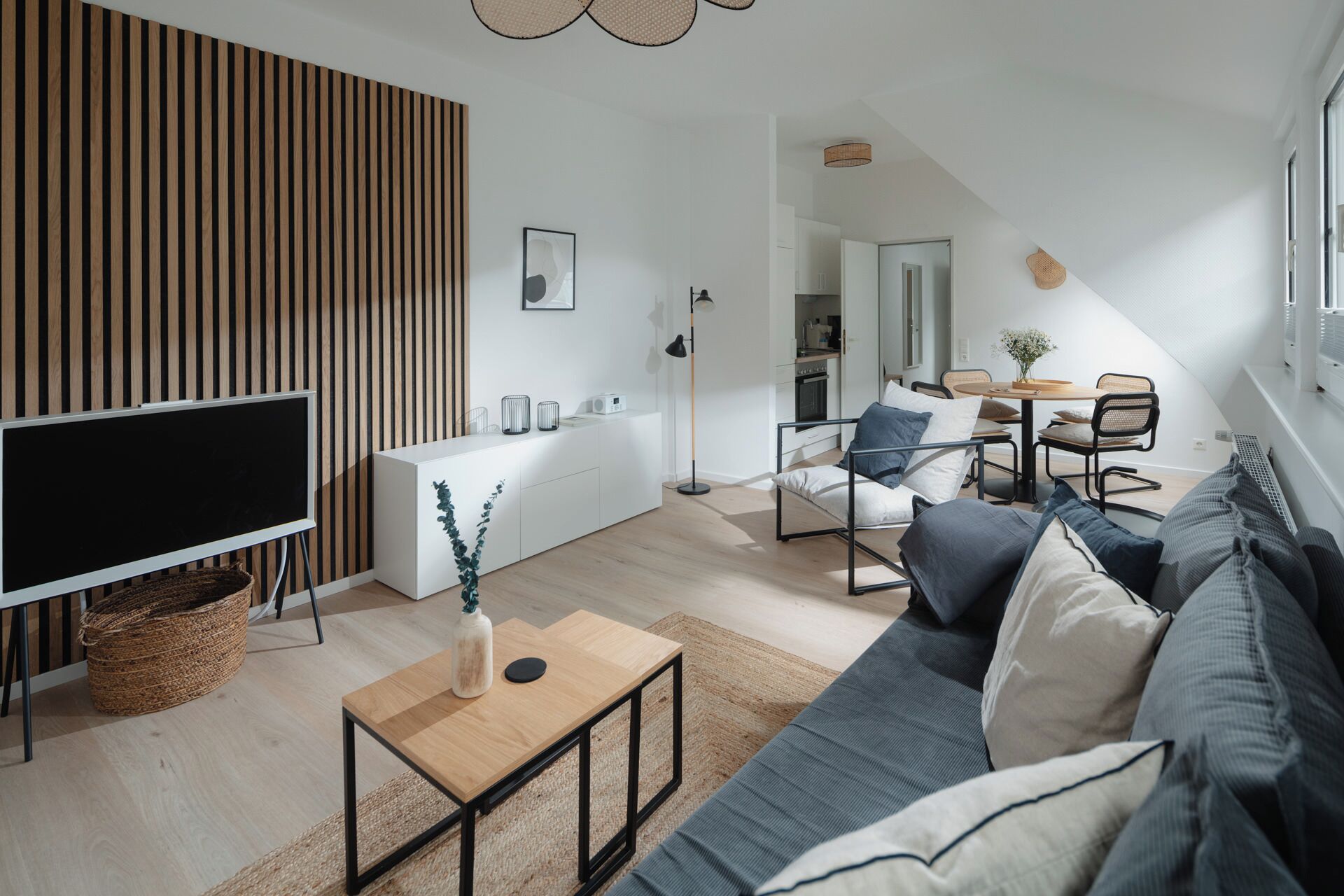 Un salon moderne avec un canapé, une table basse, un téléviseur et une cuisine en arrière-plan.