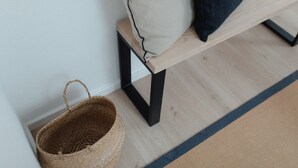 Een houten bank met een kussen en een rieten mandje tegen een muur.
