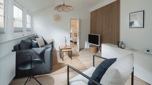Een moderne woonkamer met een bank, een fauteuil, een televisie en een wand van hout.