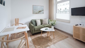 A modern living room with a green sofa, a white table, and a small white side table with a vase of flowers.