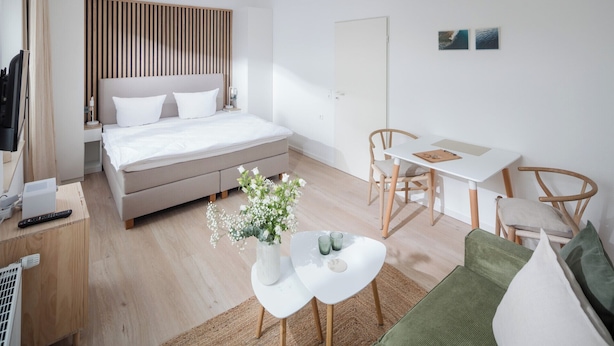A modern bedroom with a bed, bedside table, and a small white table with a vase of flowers.