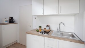 A compact kitchen with white cabinets, a wooden countertop, a built-in sink, and a coffee maker.