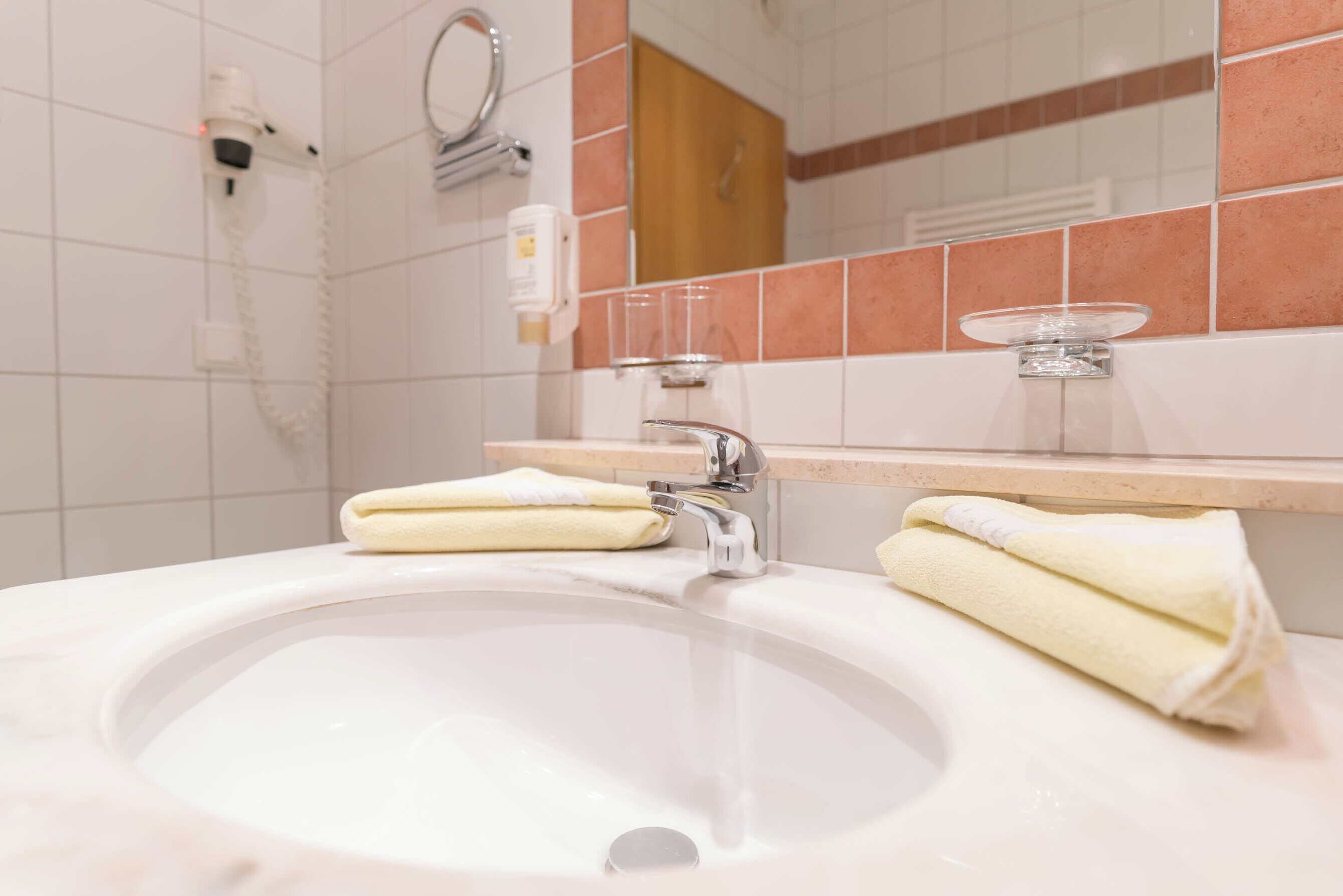 A bathroom sink with two towels, a mirror, and a hairdryer on the wall.