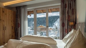 Un dormitorio con una cama grande, paneles de madera en una pared y vistas a un paisaje nevado a través de un ventanal corredero.