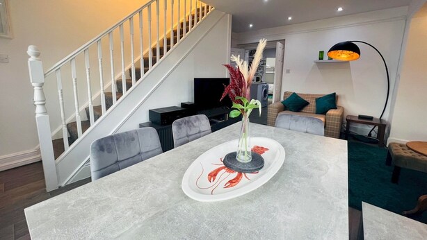 Una sala de estar moderna con un sofá gris, una mesa de comedor con un plato decorativo y una escalera que sube a otro nivel.