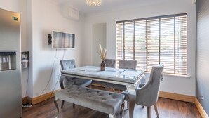 A modern dining area with a glass table, grey upholstered chairs, a bench, and a chandelier.