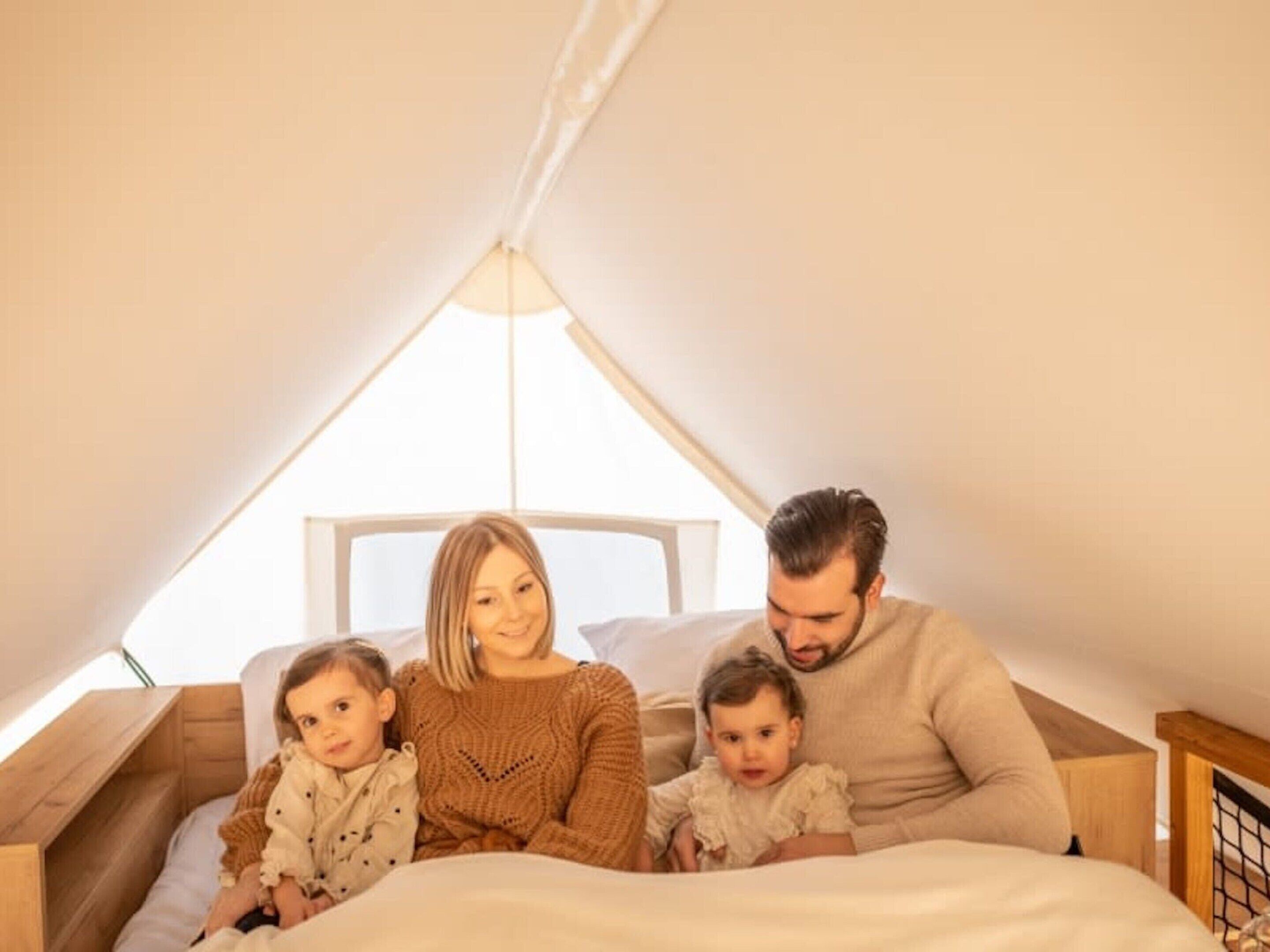 Una familia de cuatro en un acogedor dormitorio en el ático, con techo inclinado y un ventanal grande.