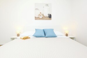 Un lit bien fait, avec une couette blanche et deux oreillers bleus, une lampe de chevet et un livre posé sur la table de chevet.