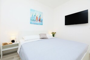 A neatly arranged bedroom with a bed, a bedside table with a lamp, a flat-screen TV mounted on the wall, and a painting above the bed. - Hedera Estate, Hedera A48 (Dubrovnik)
