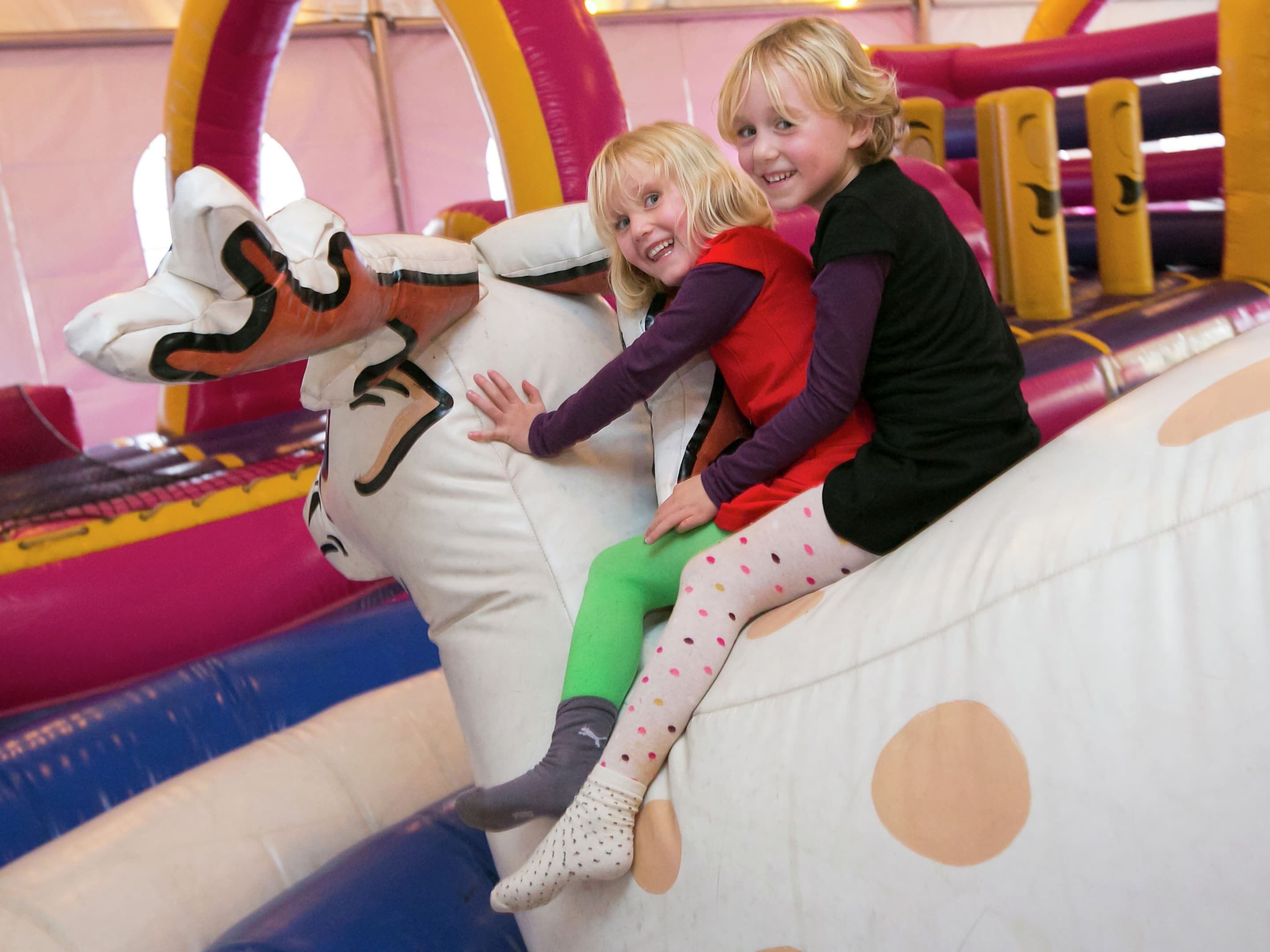 Two children on an inflatable slide with a cartoon character.